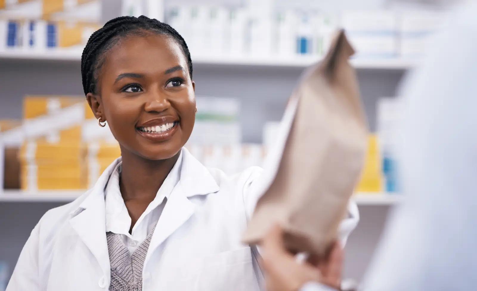 Friendly pharmacist handing a prescription bag to a patient at a pharmacy counter.