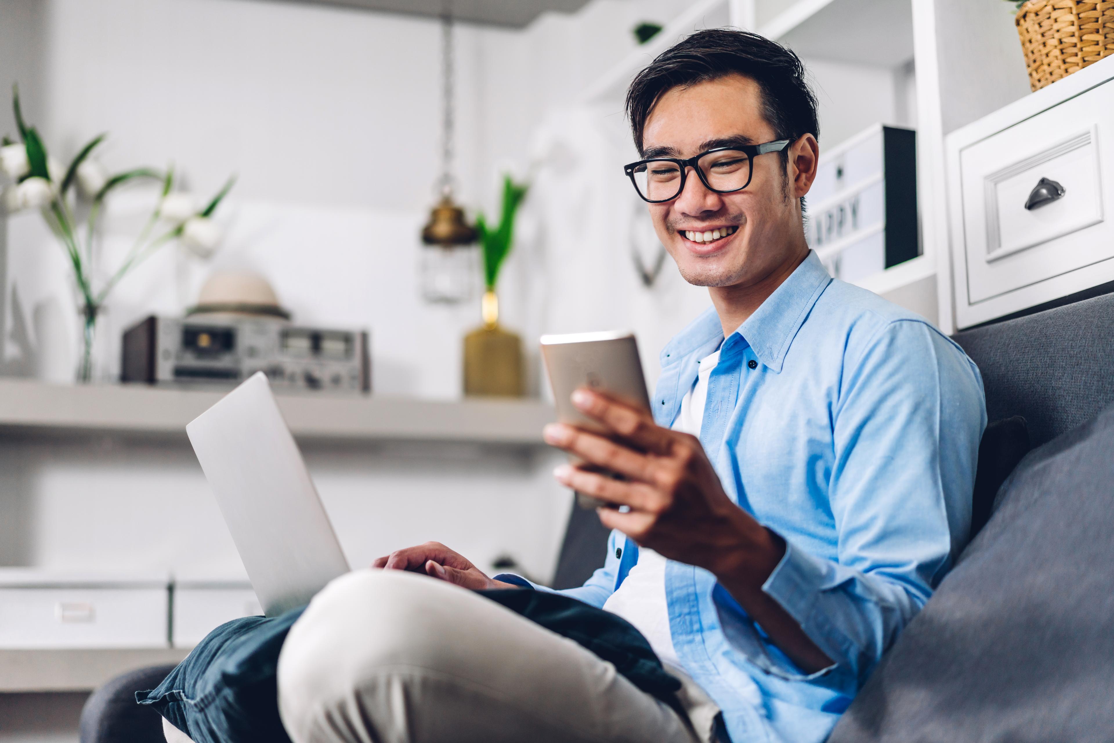 Young smiling asian person using laptop computer working and and looking at phone