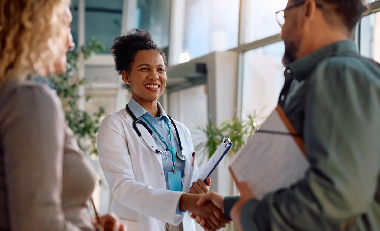 Friendly doctor greeting patients with a handshake and smile in a bright medical facility lobby.