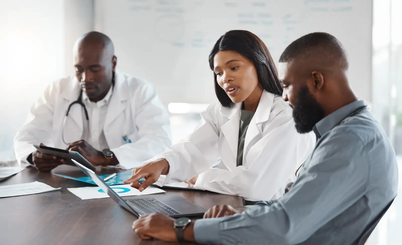 Medical professionals collaborating in a meeting, analyzing data and discussing healthcare strategy using laptops and tablets.
