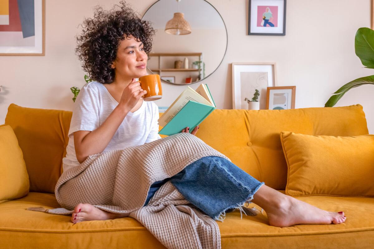 Biller sits on couch at home drinking coffee and reading medical billing books