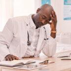 Physician sitting at desk with hand in head experiencing cardiologist burnout