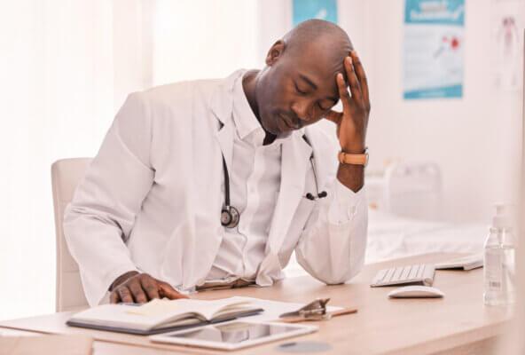 Physician sitting at desk with hand in head experiencing cardiologist burnout
