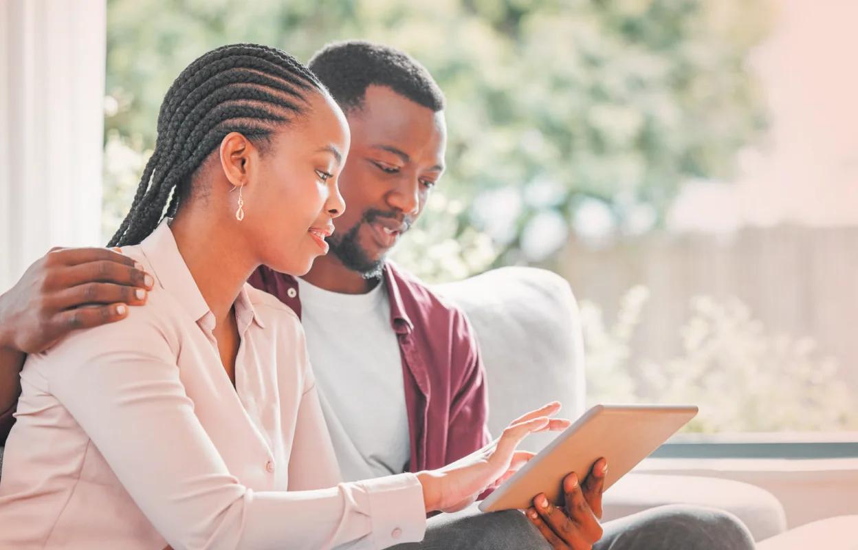 A couple sitting together on a couch, reviewing healthcare information on a tablet in a bright living room.