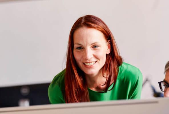 This is an image of a woman looking at a computer screen with a colleague and smiling. This is meant to represent someone who is happy about their medical claims process.