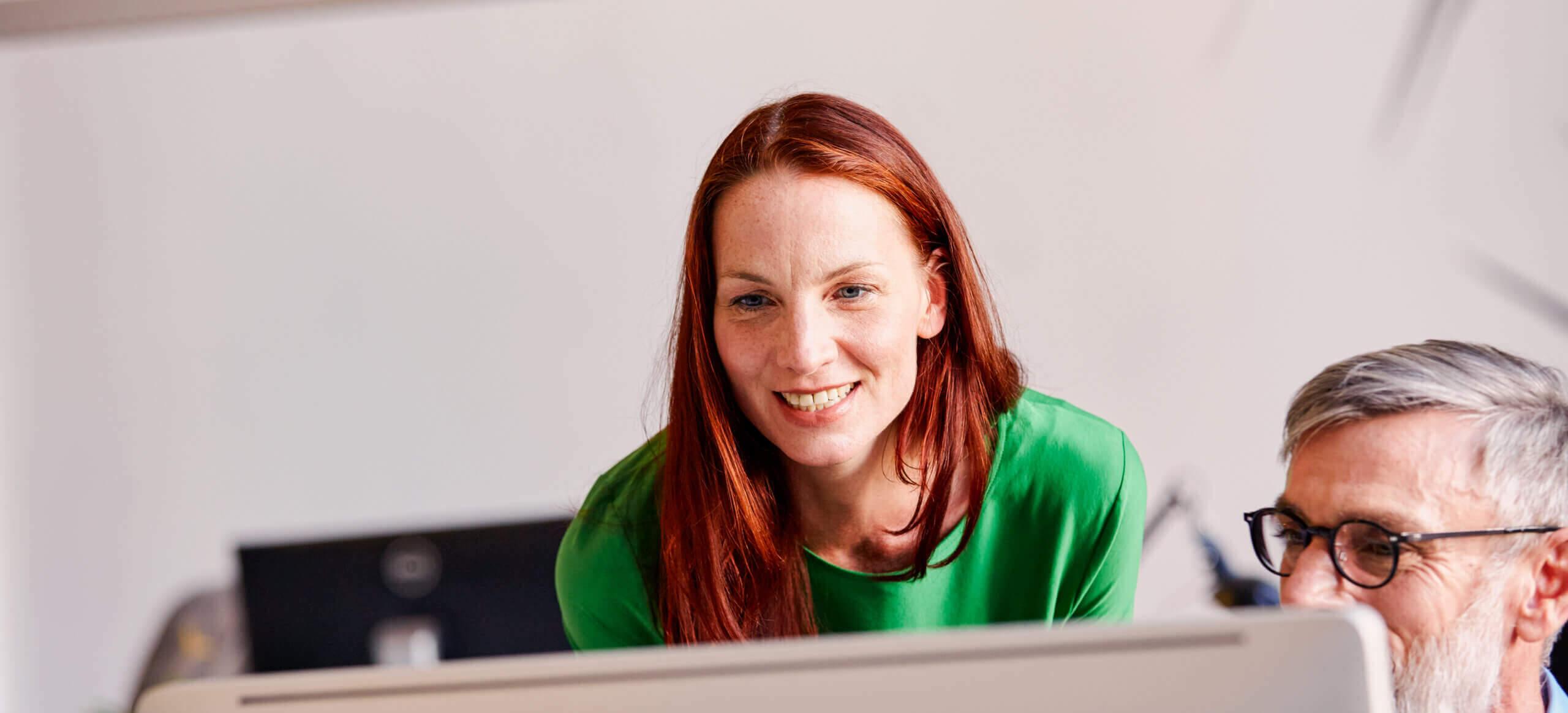 This is an image of a woman looking at a computer screen with a colleague and smiling. This is meant to represent someone who is happy about their medical claims process.