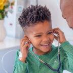 A Black child trying on a stethoscope with a Black doctor and a parent to illustrate a successful doctor's visit for a child with autism