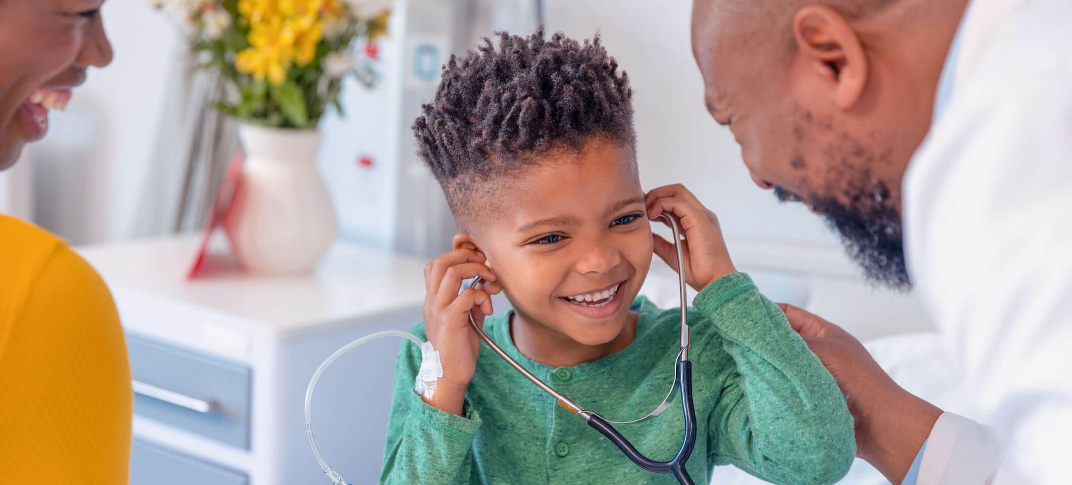 A Black child trying on a stethoscope with a Black doctor and a parent to illustrate a successful doctor's visit for a child with autism
