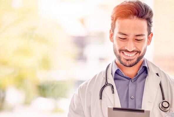 Physician smiles while holding tablet looking for healthcare thought leaders to follow on social media