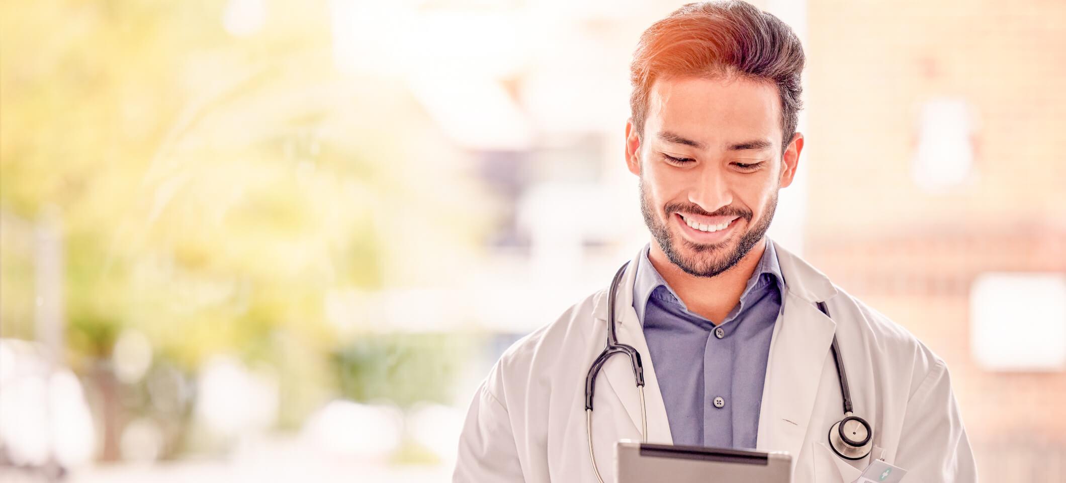 Physician smiles while holding tablet looking for healthcare thought leaders to follow on social media