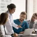 Medical professionals gathered in a meeting discussing patient care and practice strategies around a laptop in a hospital office.