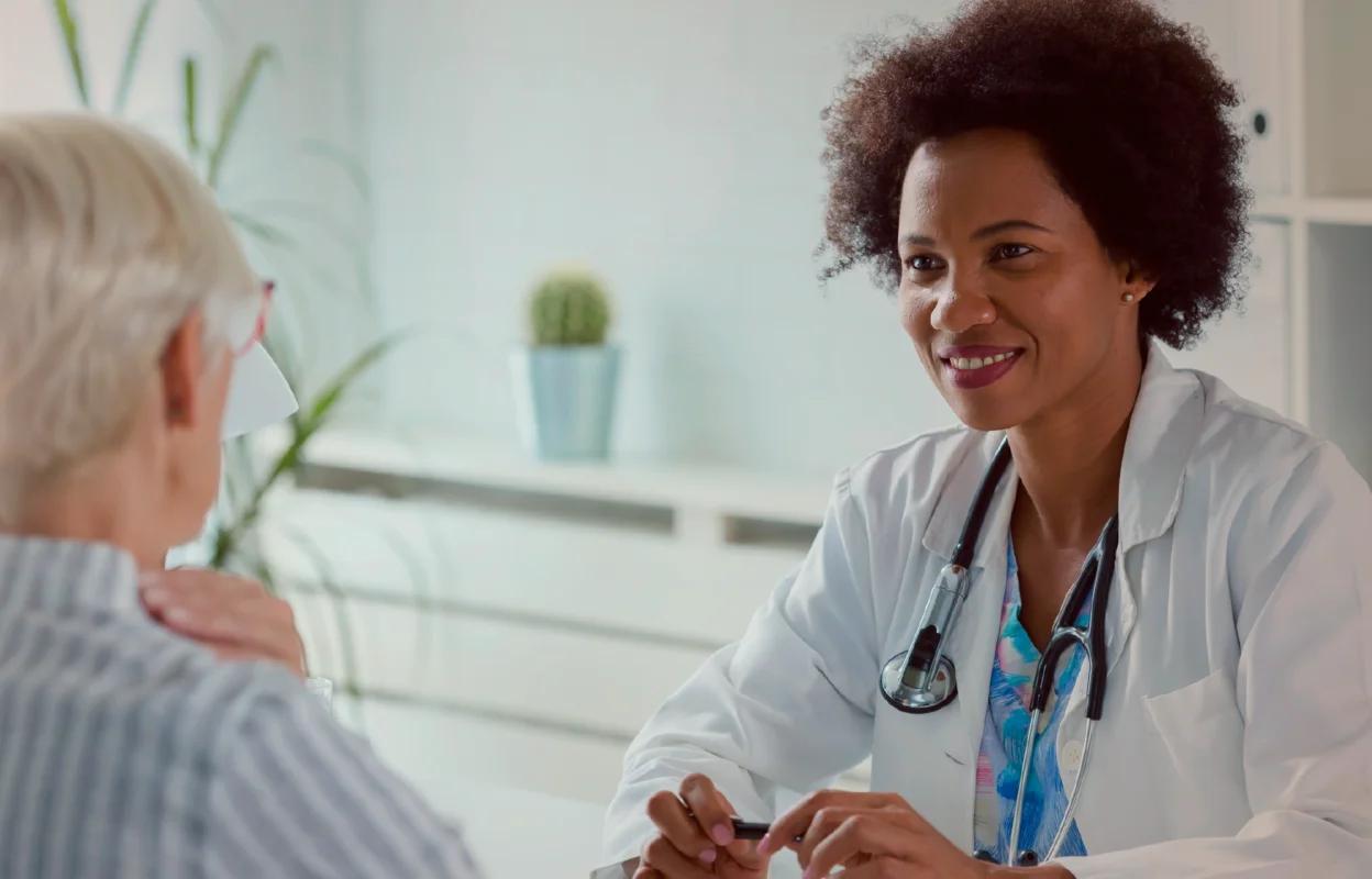 Smiling female doctor with a stethoscope talks to an older woman patient in a medical office.